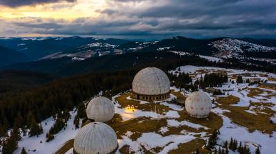 Aerial view of several large geodesic dome structures on a snowy, mountainous landscape under a cloudy sky at sunset.