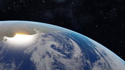 View of Earth from space showing clouds over the ocean, with sunlight illuminating part of the land near the planet's curved horizon against a dark space background.